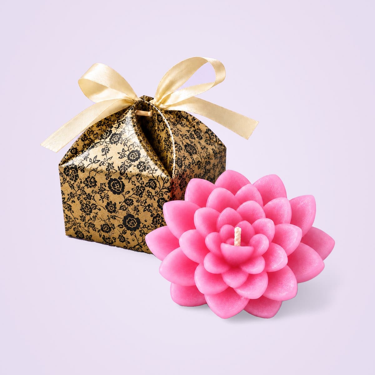 Pink lotus candle beside its gold gift box printed with black roses