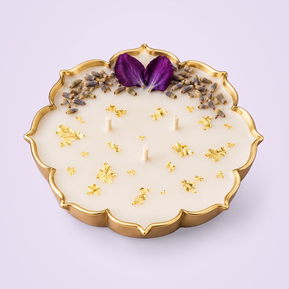 Metal urli candle in a shallow eight-lobed gold tin, with dried purple petals and lavender at one edge and gold flakes