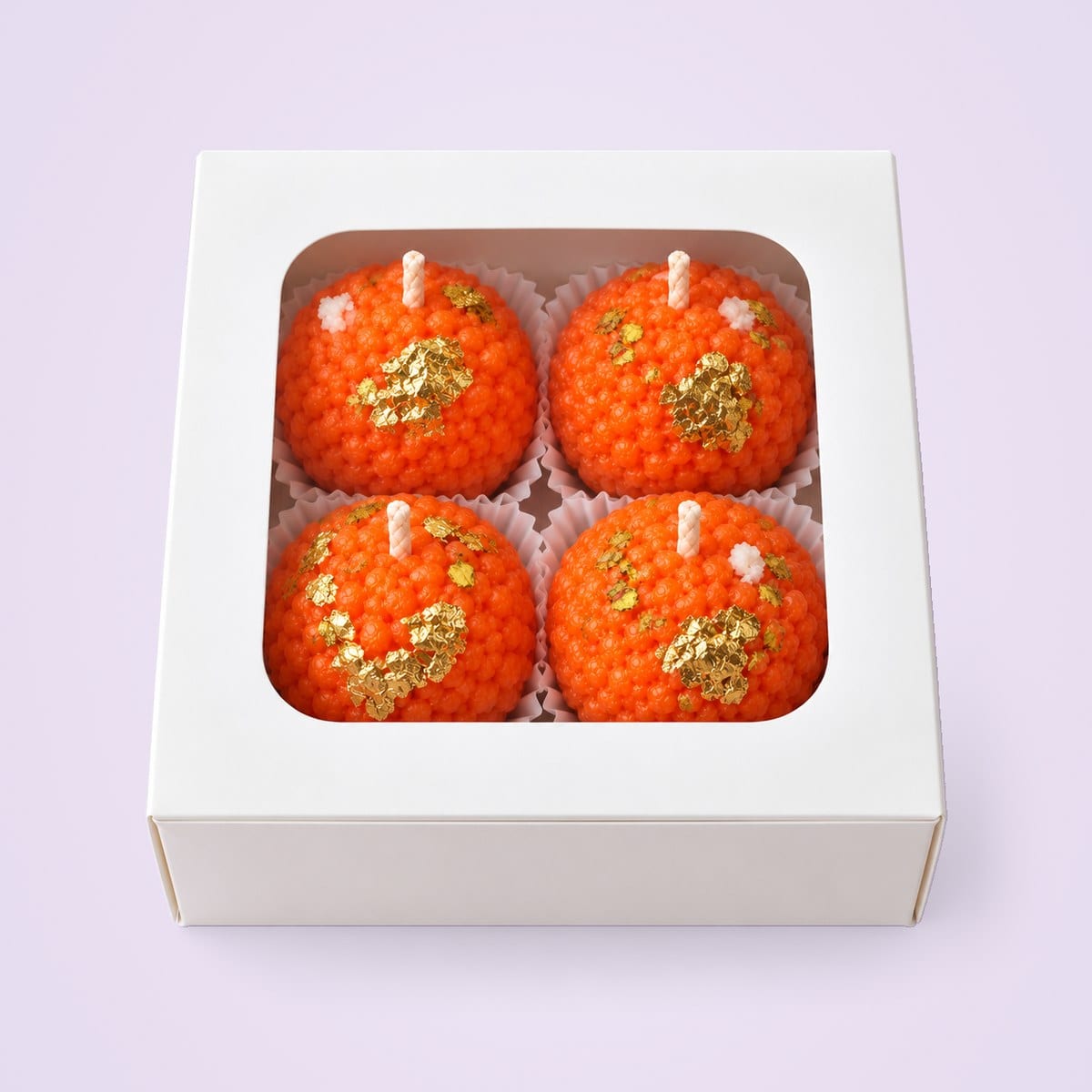 Four orange motichoor laddu candles in a closed white box with a window