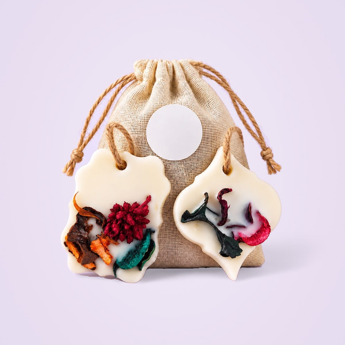 Two ivory soy wax sachets with dried botanicals and a jute pouch